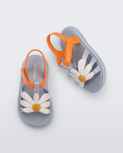 Top and side view of a pair of blue baby Hip Bloomy sandal with orange strap and white flower