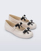 Angled view of a pair of beige Soft Ballerina Bow flats with black bows and a pearl in the center of each bow