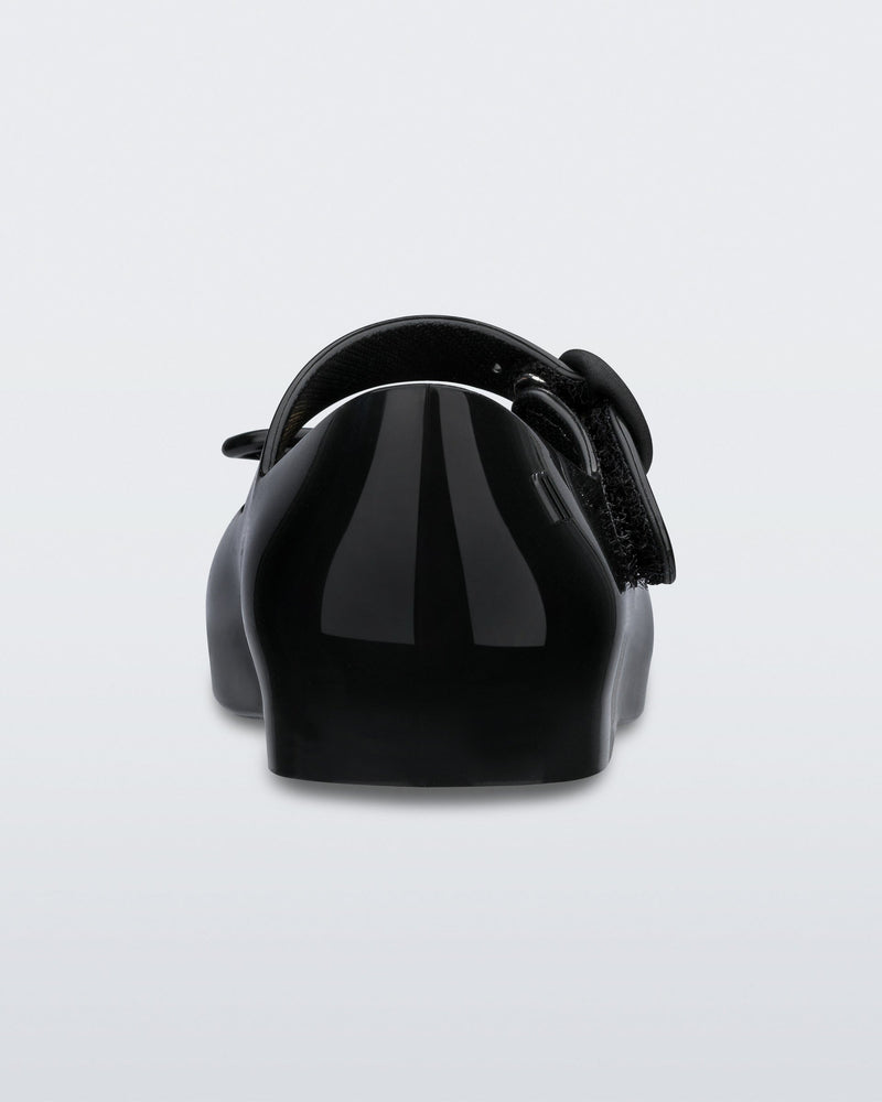 Back view of a black Mini Melissa Sweet Love flat with a top strap and a bow detail on the toe.