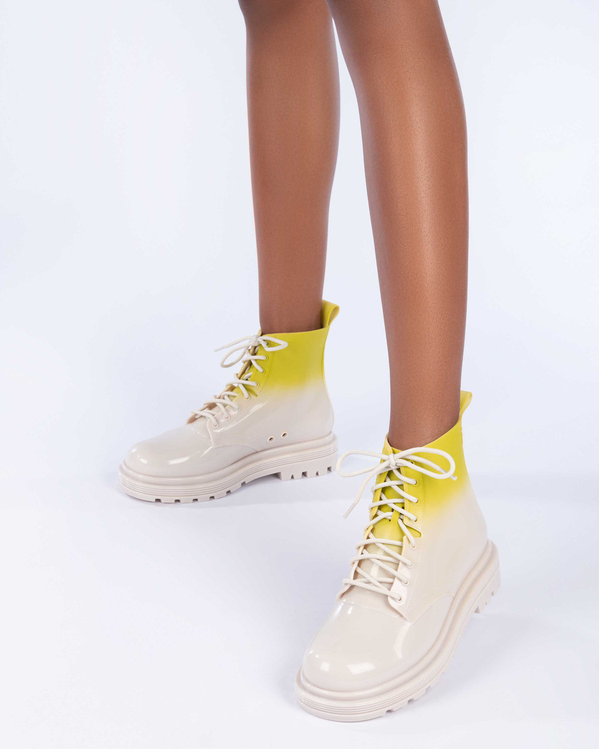 A model's legs wearing a pair of beige/green Melissa Coturno boots with a green into beige ombre base, beige laces and sole.
