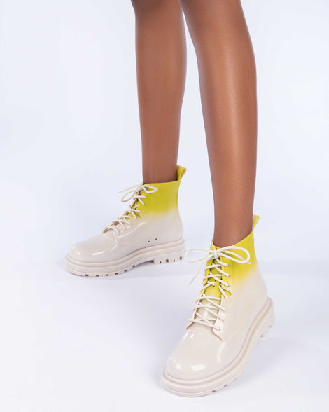 A model's legs wearing a pair of beige/green Melissa Coturno boots with a green into beige ombre base, beige laces and sole.
