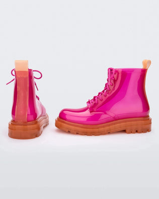 A back and side view of a pair of clear orange / pink Melissa Coturno boots with a pink base, laces and an orange sole.