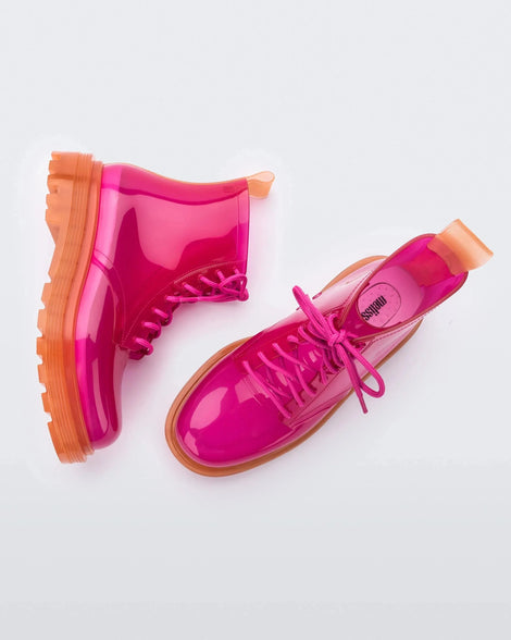A top and side view of a pair of clear orange / pink Melissa Coturno boots with a pink base, laces and an orange sole.