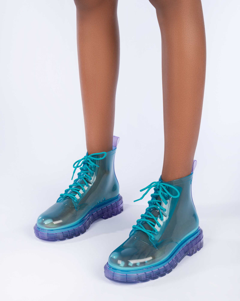 A model's legs wearing a pair of clear lilac/blue Melissa Coturno boots with a transparent blue base, laces and a lilac sole.
