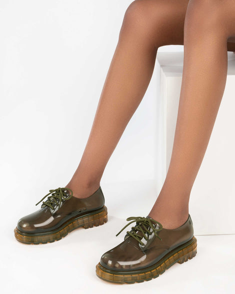 A model's legs wearing a pair of clear green / yellow Melissa Bass sneakers, with a transparent green base, green laces and a transparent yellow sole.