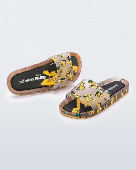 An angled front and top vew of a pair of clear beige / yellow Mini Melissa Beach slides with a beige base and a pattern of Disney's Pluto the dog with different facial expressions.