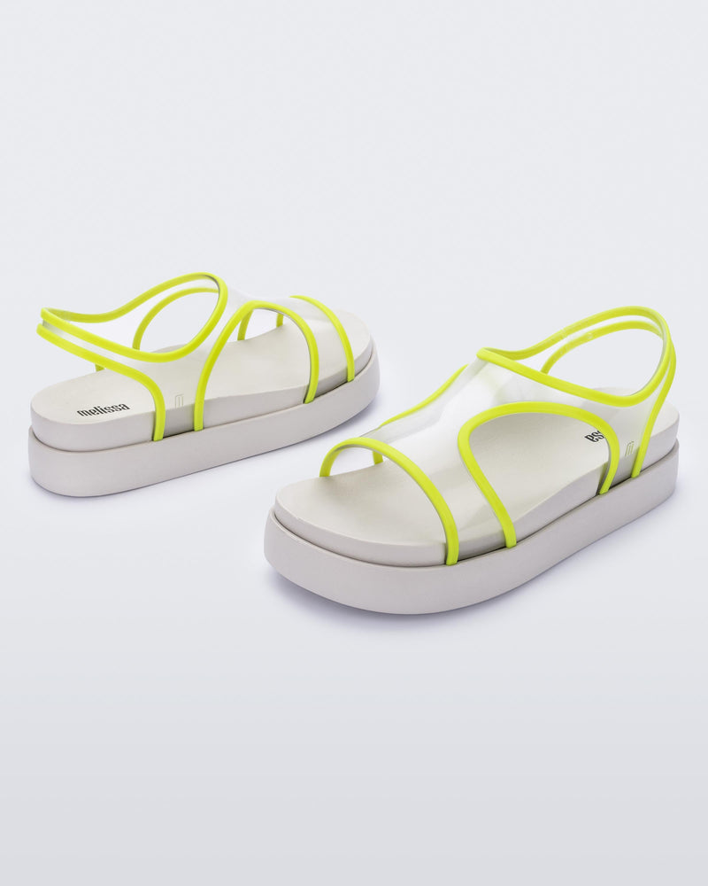 An angled front and side view of a pair of beige/green Melissa Bikini platform sandals with two transparent green straps conjoining in the middle and a beige sole.