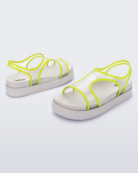 An angled front and side view of a pair of beige/green Melissa Bikini platform sandals with two transparent green straps conjoining in the middle and a beige sole.