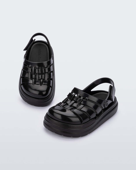 An angled front and top view of a pair of black Mini Melissa Sunday sandals with woven closed toe front and back ankle strap.