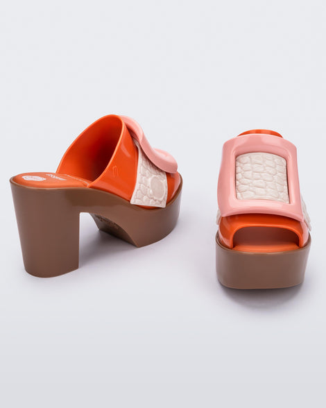 Angled view of a pair of orange/brown Melissa Buckle Up heeled mules with ivory strap and pink buckle.