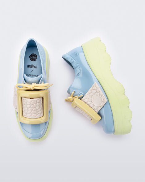 Top and side view of a pair of blue Melissa Buckle Up Kick Off platform sneaker with green platform sole and a yellow buckle and ivory strap.