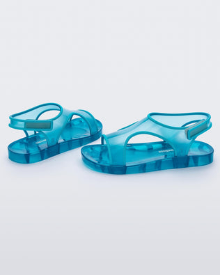 An inner and outter side view of a pair of translucent blue Mini Melissa Aqua sandals with two straps cojoining in the middle and a velcro back strap.