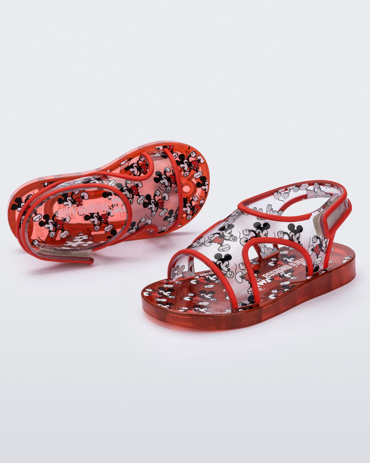 Angled view of a pair of red Mini Melissa Acqua sandals with Mickey Mouse print
