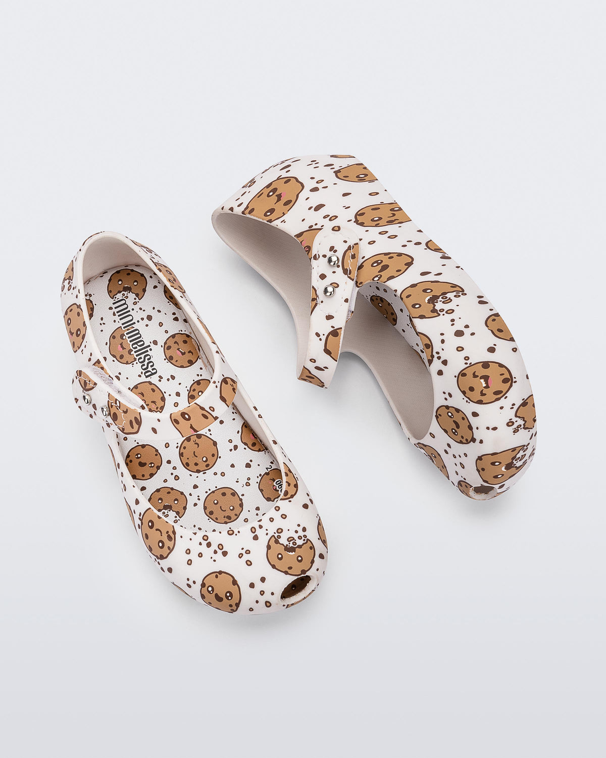 Top and side view of the Mini Melissa Ultragirl flats in candy print. The print is an all over white / beige chocolate chip cookie print. The shoe has a single velcro strap across the front of the foot. 