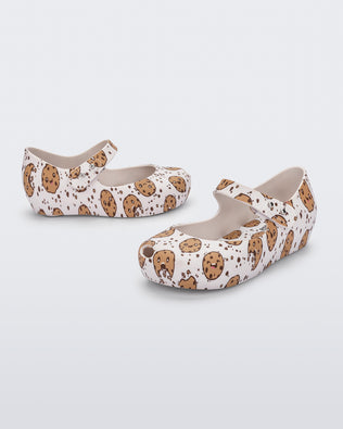Angled view of a pair of Mini Melissa Ultragirl flats in candy print. The print is an all over white / beige chocolate chip cookie print. The shoe has a single velcro strap across the front of the foot. 