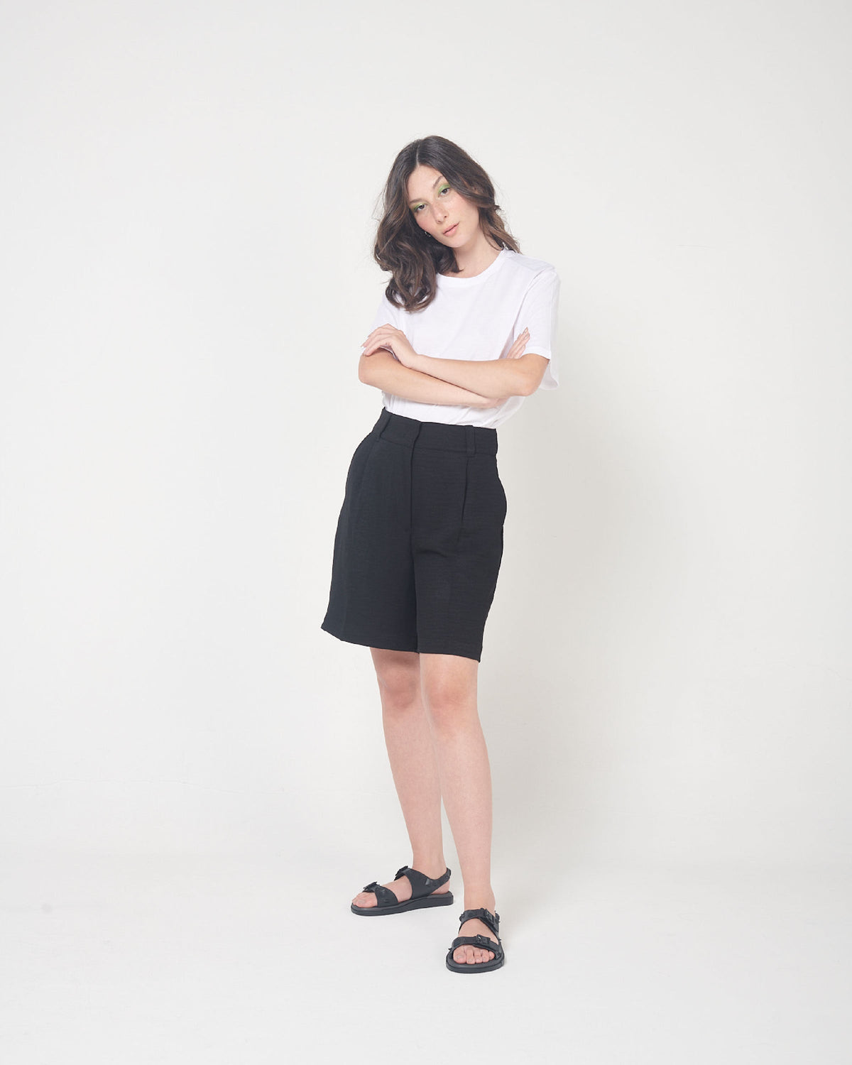 A model posing for a picture in a white top, black bottoms and a pair of black Melissa Spikes Sandals with two straps with buckles on top and spike details around the base.