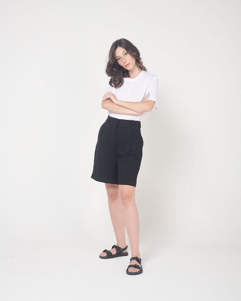A model posing for a picture in a white top, black bottoms and a pair of black Melissa Spikes Sandals with two straps with buckles on top and spike details around the base.