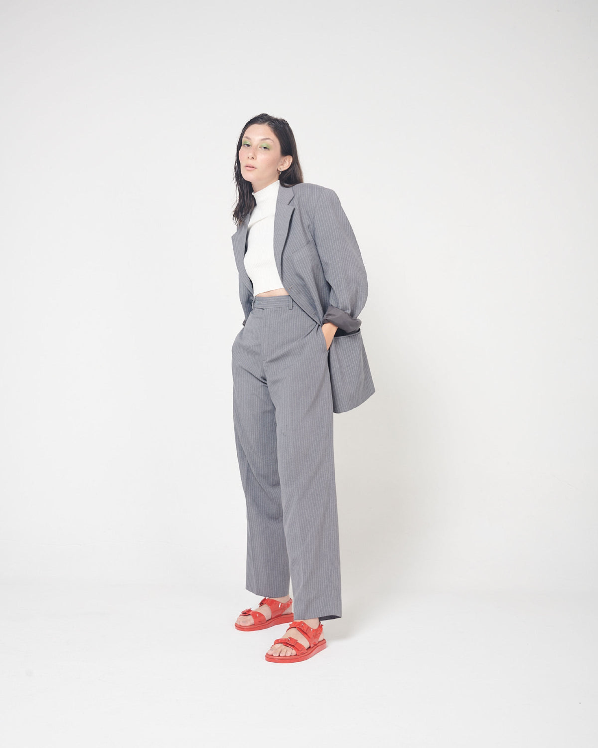 A model posing for a picture in a gray suit and a pair of red Melissa Spikes Sandals with two straps with buckles on top and spike details around the base.