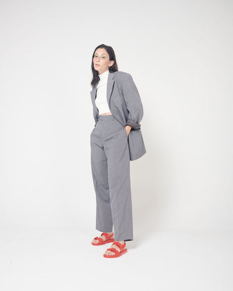 A model posing for a picture in a gray suit and a pair of red Melissa Spikes Sandals with two straps with buckles on top and spike details around the base.