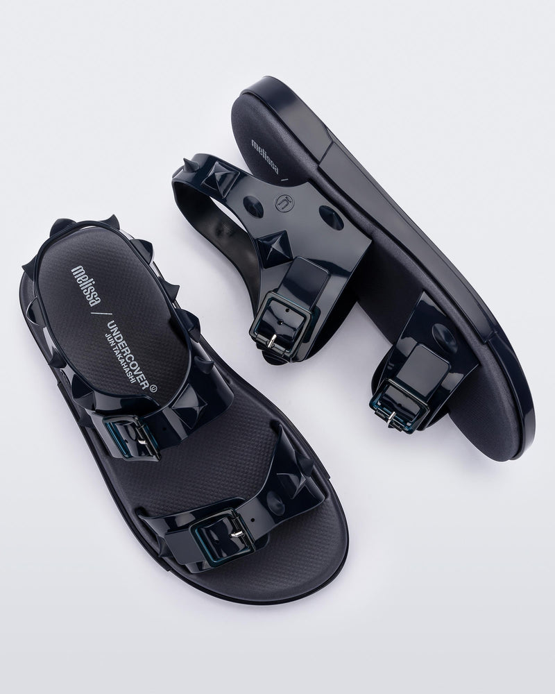 A top and side view of a pair of blue Melissa Spikes Sandals with two straps with buckles on top and spike details around the base.