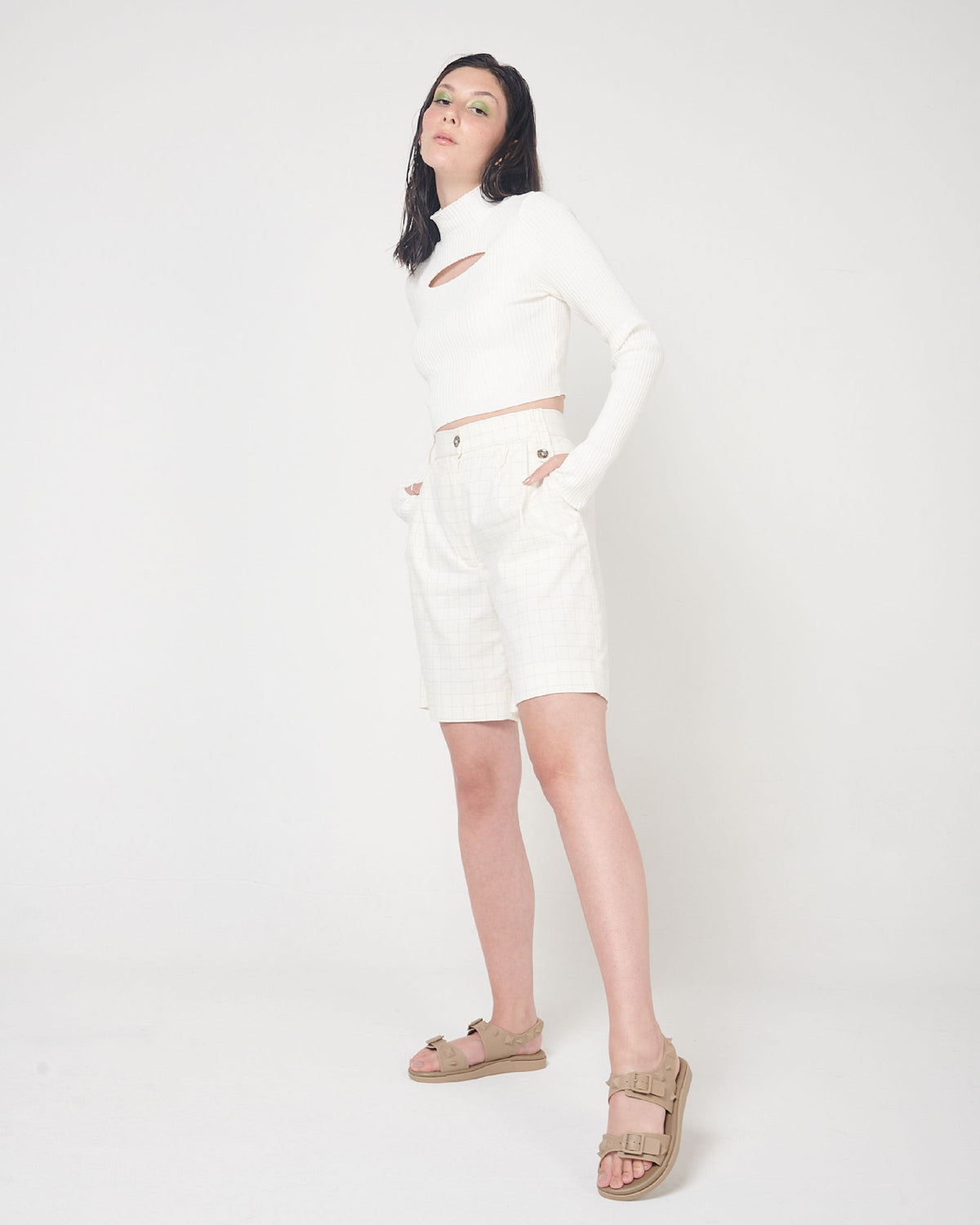 A model in a white top and bottoms and a pair of beige Melissa Spikes Sandals with two straps with buckles on top and spike details around the base.