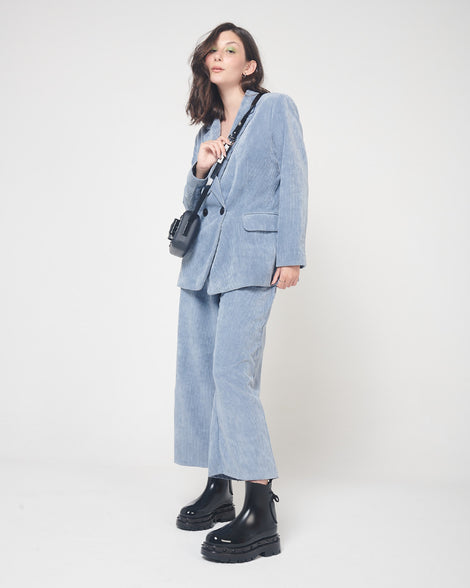 A model posing for a picture in a blue corduroy suit, a purse on her shoulder and a pair of black Melissa Spikes Boots with spike details around the sole and laces in the back.
