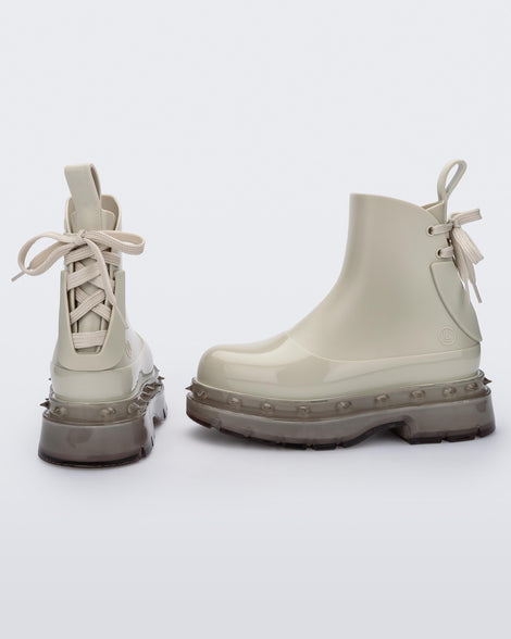 An angled side and back view of a pair of beige Melissa Spikes Boots with spike details around the sole and laces in the back.