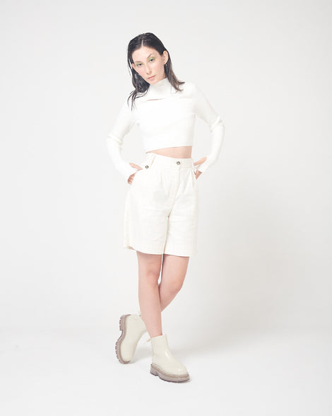 A model posing for a picture in a white top, white bottoms and a pair of beige Melissa Spikes Boots with spike details around the sole and laces in the back.