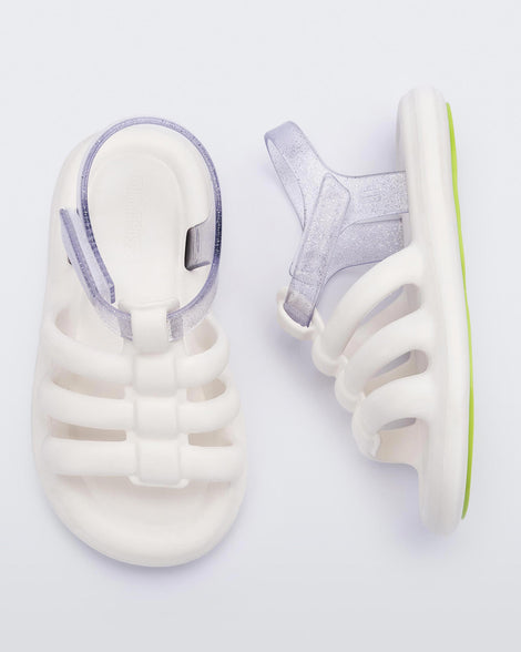 Top and side view of a pair of white Mini Melissa Freesherman sandals white and clear glitter straps.