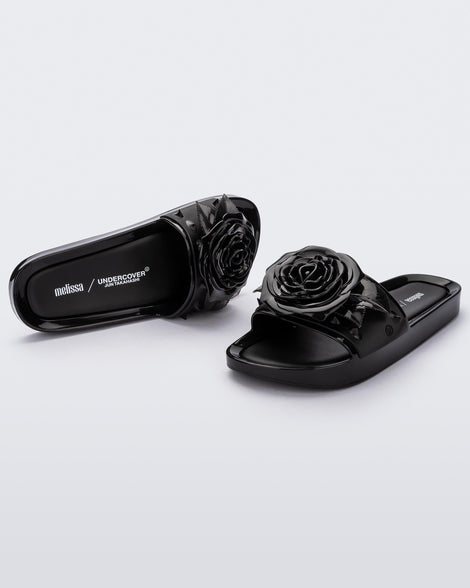 An angled front and side view of a pair of black Melissa Spikes Beach slides with a flower detail and spikes on the front strap.