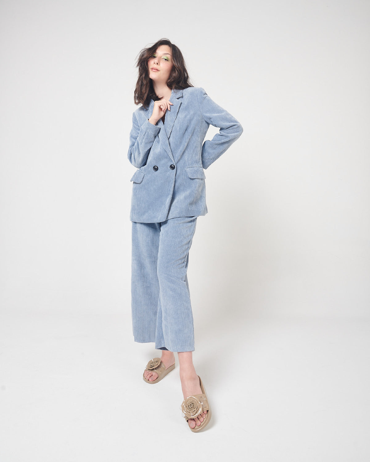 A model in a blue corduroy suit and a pair of beige Melissa Spikes Beach slides with a flower detail and spikes on the front strap.