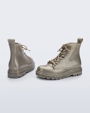 Angled view of a pair of Mini Melissa lace up Coturno boots in gold glitter color-way