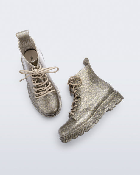 Top and side view of a pair of Mini Melissa lace up Coturno boots in gold glitter color-way