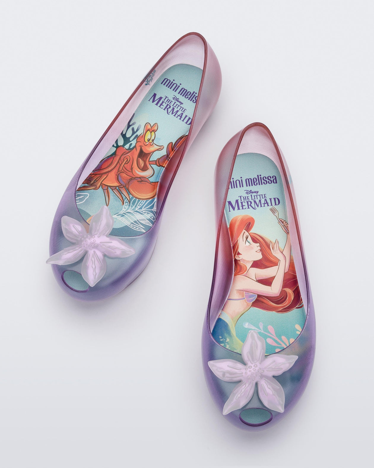 Top view of a pair of clear pearly pink and purple Mini Melissa Ultragirl + Disney Little Mermaid flats with a pearly purple flower.