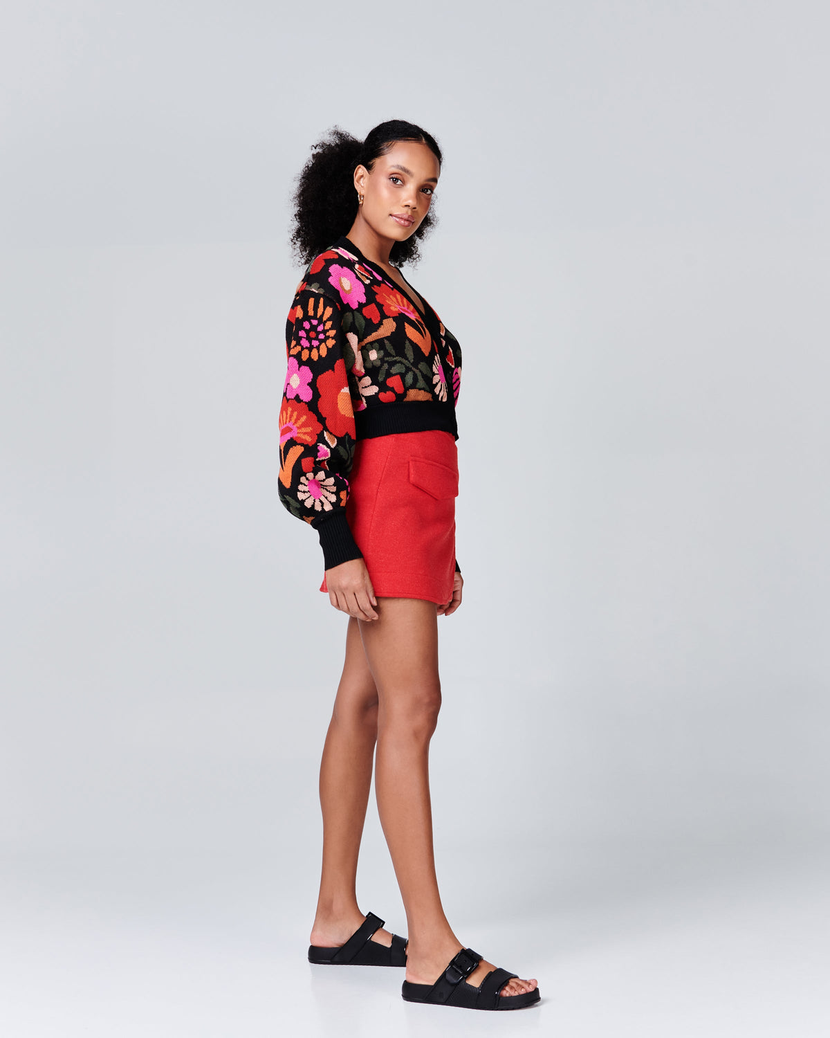 Model in a red skirt and black patterned sweater wearing a pair of black Cozy Connection slides
