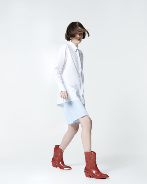Model in a white shirt and long jean shorts wearing a pair of red Texas boots.