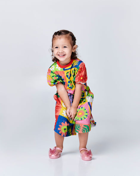 Child model in a multi colored dress wearing a pair of pink Sweet Love Butterfly baby flats
