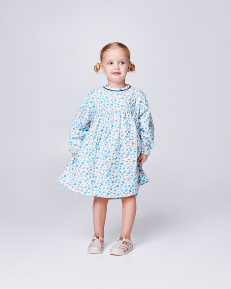 Child model in a white dress with blue flower print wearing a pair of Metallic beige Hip Daydream baby sandals
