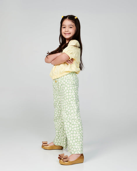 Child model in a yellow shirt and green floral pants wearing a pair of pearly beige kids Ultragirl Classic Bow kids flats
