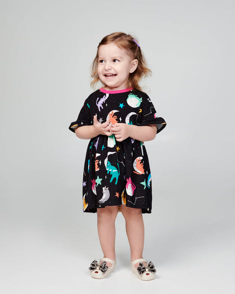 Child model in a black patterned dress wearing a pair of beige baby Ultragirl Classic Bow flats with black and clear bow