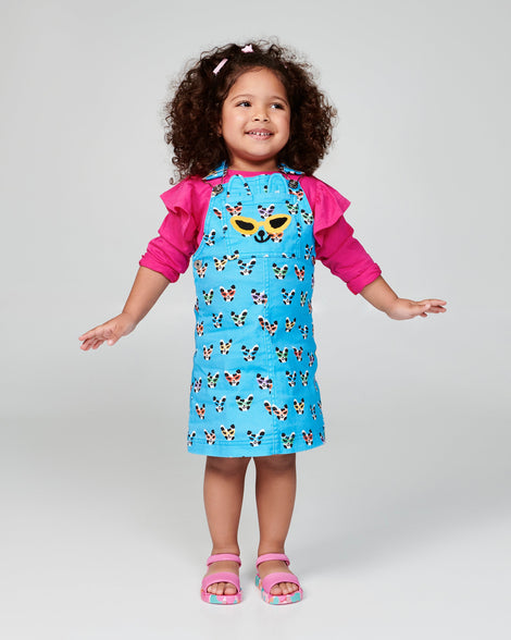 Child model in a blue dress wearing  a pair of pink baby Imagine sandals