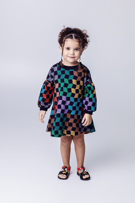 Child model in a black multi-colored dress wearing a pair of black  Play Mickey & Minnie sandals with red straps
