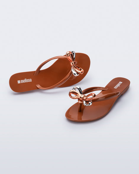 Top and angled view of a pair of brown Harmonic Eclipse flip flops with bow. 