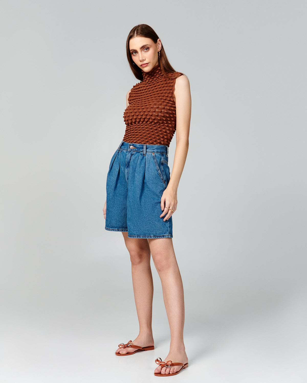 Model in a brown shirt and jean shorts wearing a pair of brown Harmonic Eclipse flip flops with bow.