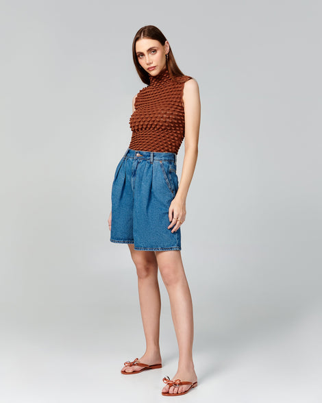 Model in a brown shirt and jean shorts wearing a pair of brown Harmonic Eclipse flip flops with bow.