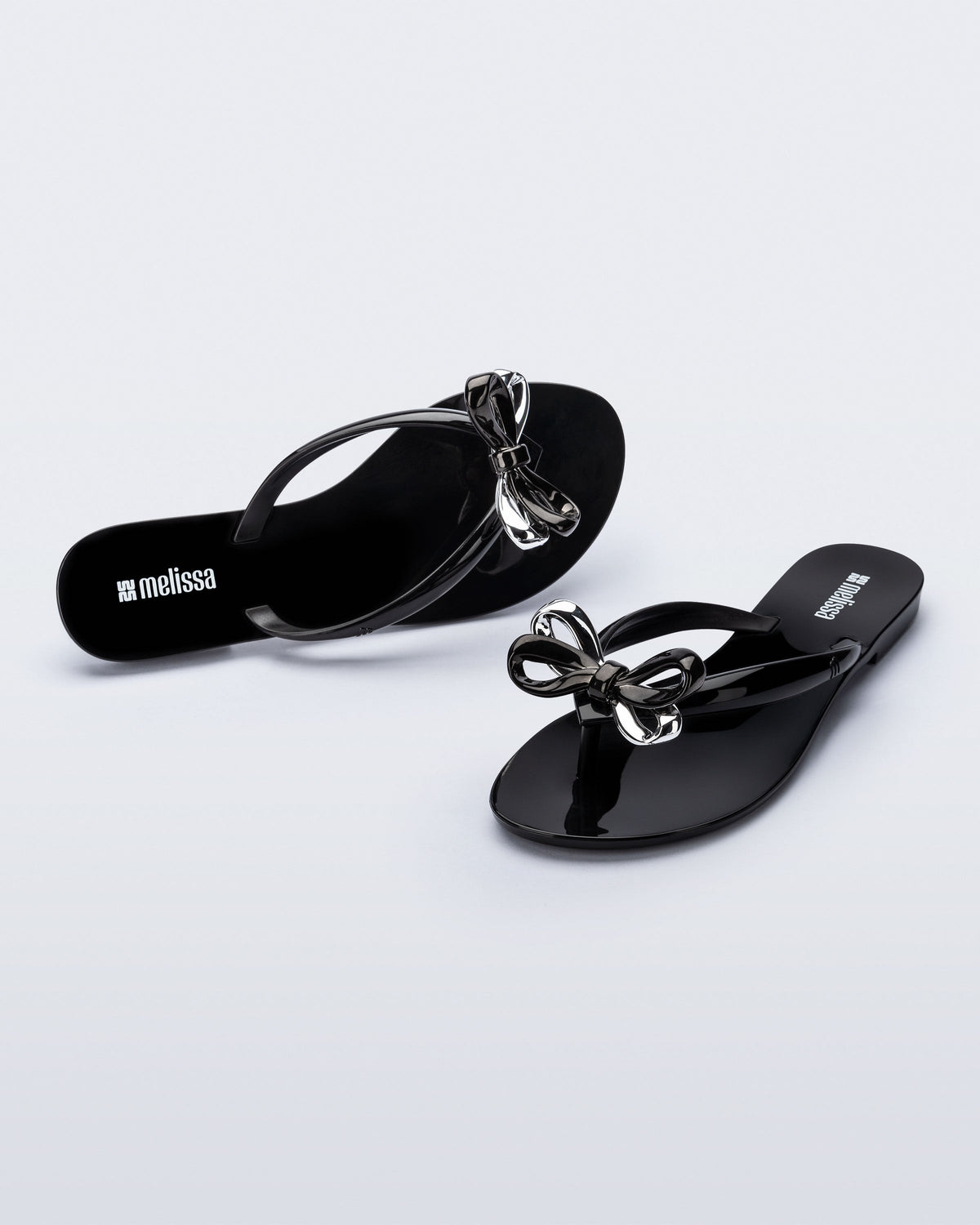 Top and angled view of a pair of black Harmonic Eclipse flip flops with bow.