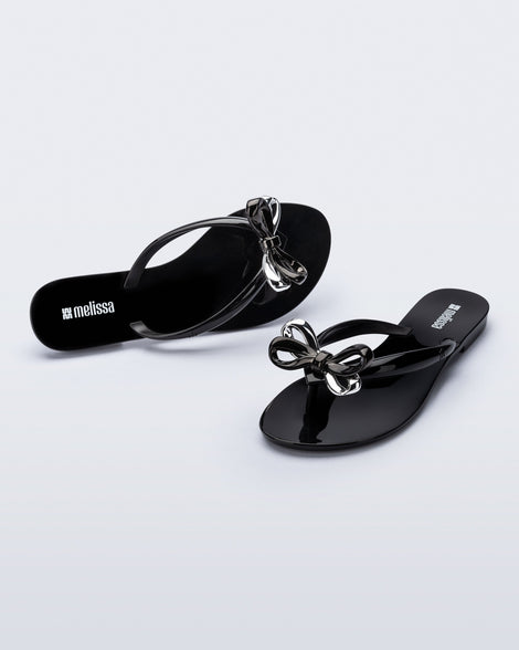 Top and angled view of a pair of black Harmonic Eclipse flip flops with bow.