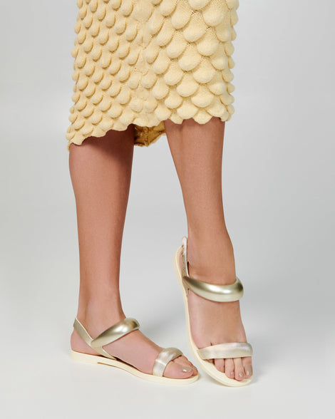 Model's legs in a pair of beige Eclipse Sandals with gold straps.