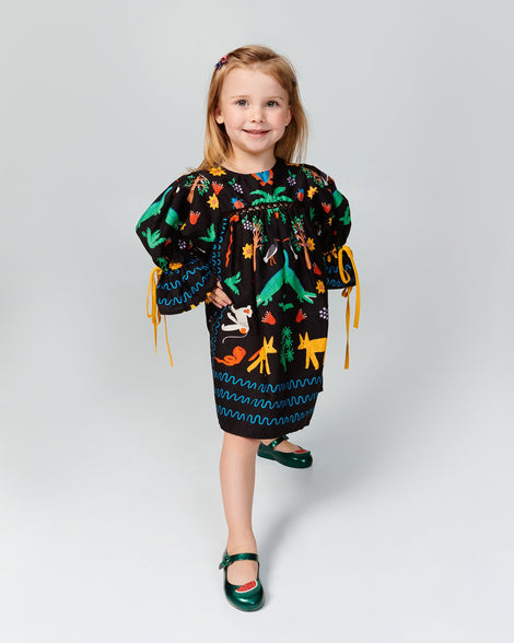 Child model in a black patterned dress wearing a pair of green Sweet Love Picnic baby flats with watermelon slices