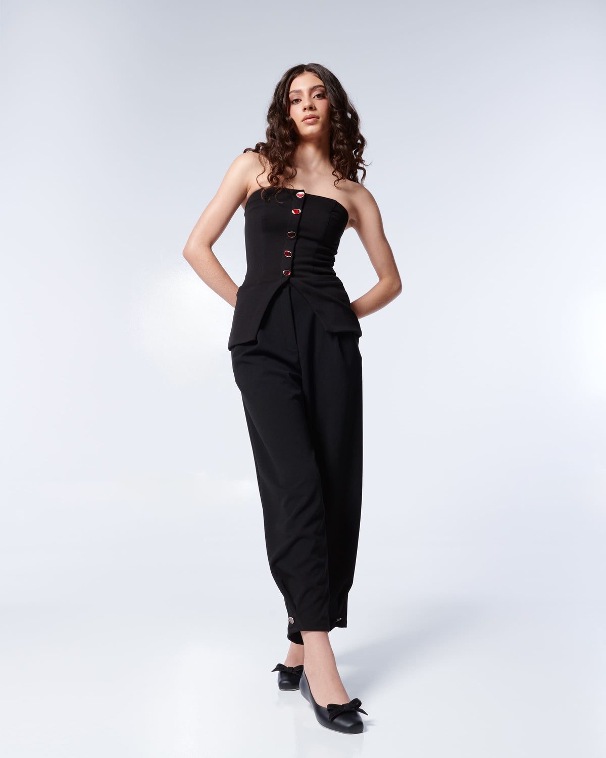 Woman posing wearing a black strapless jumpsuit with red buttons and the Melissa Aura flats in black. 